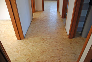 OSB Platten als Grundlage in der Altbausanierung. Zu sehen ist ein Vorsaal mit angrenzenden Zimmern. Die Platten sind unbehandelt und dienen als Untergrund für einen Bodenbelag oder auch zur Versiegelung.